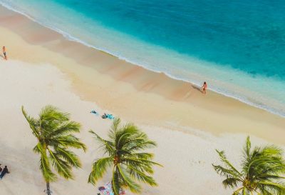 A vibrant tropical beach scene with people, palms, and turquoise waters from above.