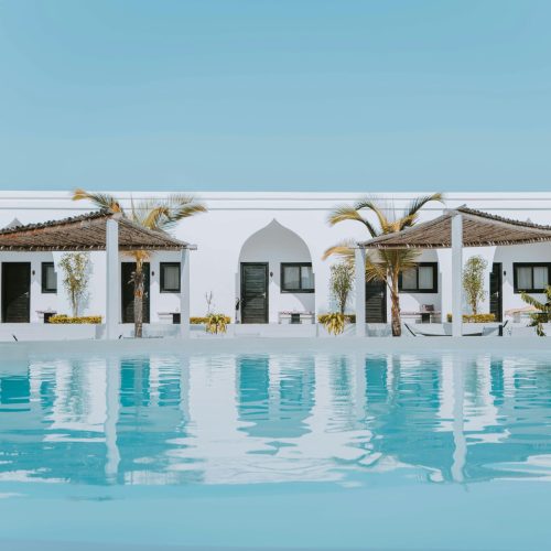 Elegant white villa in Zanzibar featuring a stunning swimming pool and palm trees under a blue sky.